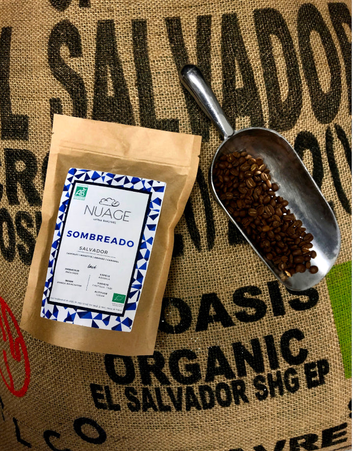 Sachet de café de spécialité bio Sombreado posé sur un sac de jute avec des grains de café – torréfaction artisanale à Hem, pour professionnels et particuliers, Nuage Coffee Roasters
